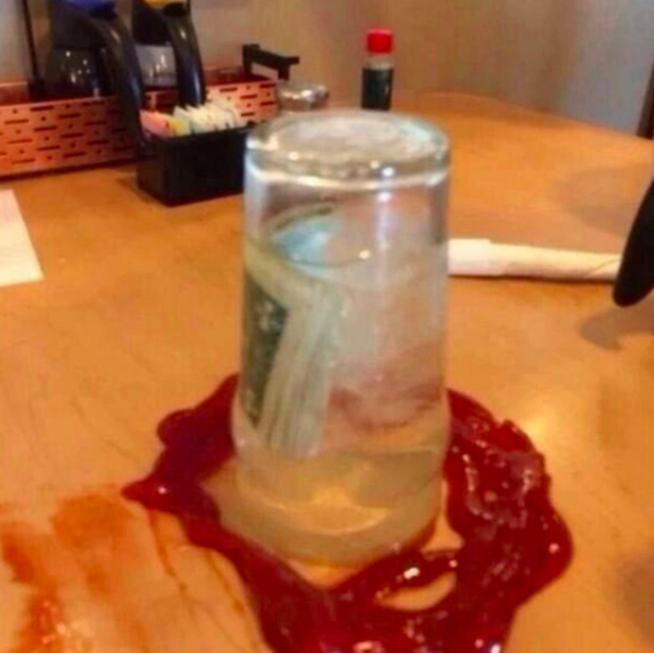 Tip money left in glass of water with ketchup around it