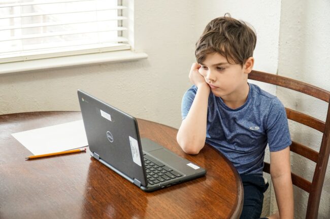 boy in blue crew neck t-shirt using macbook pro on brown wooden table