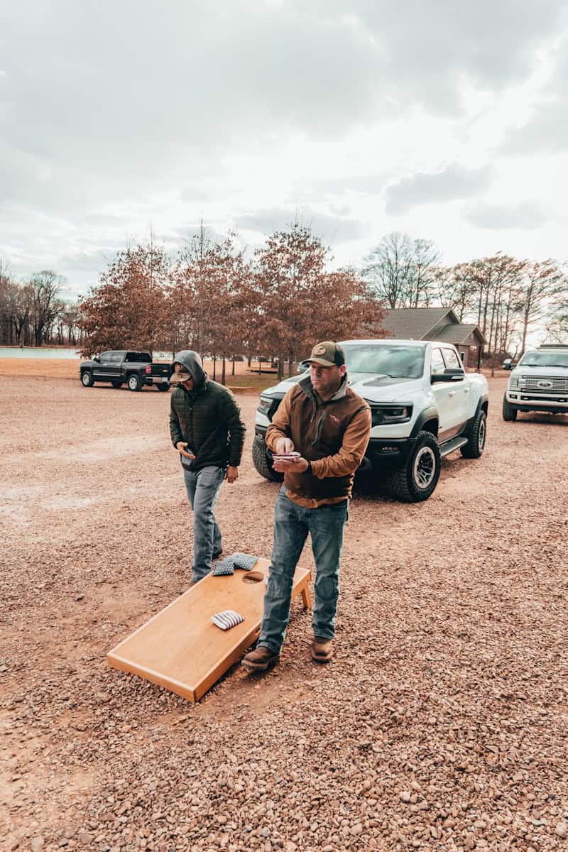 a couple of men standing on a wood board in a dirt field