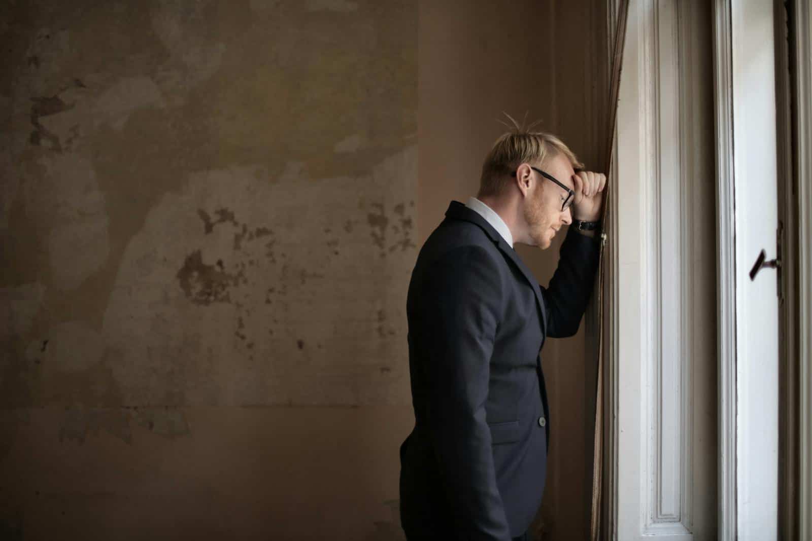 A worried businessman in a suit leaning against a window, expressing stress and concern.