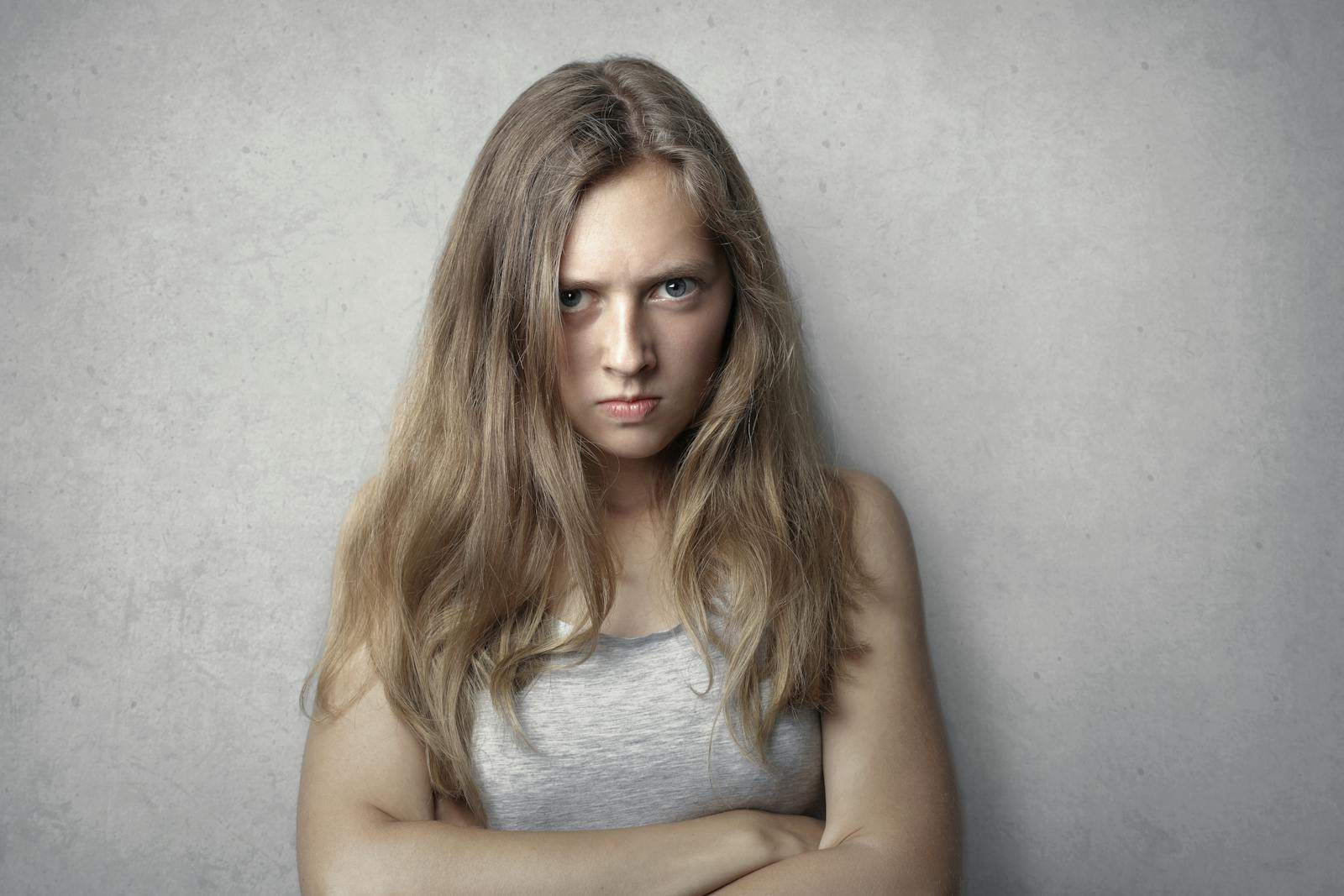 Portrait of a fierce woman with crossed arms and intense expression on a gray background.