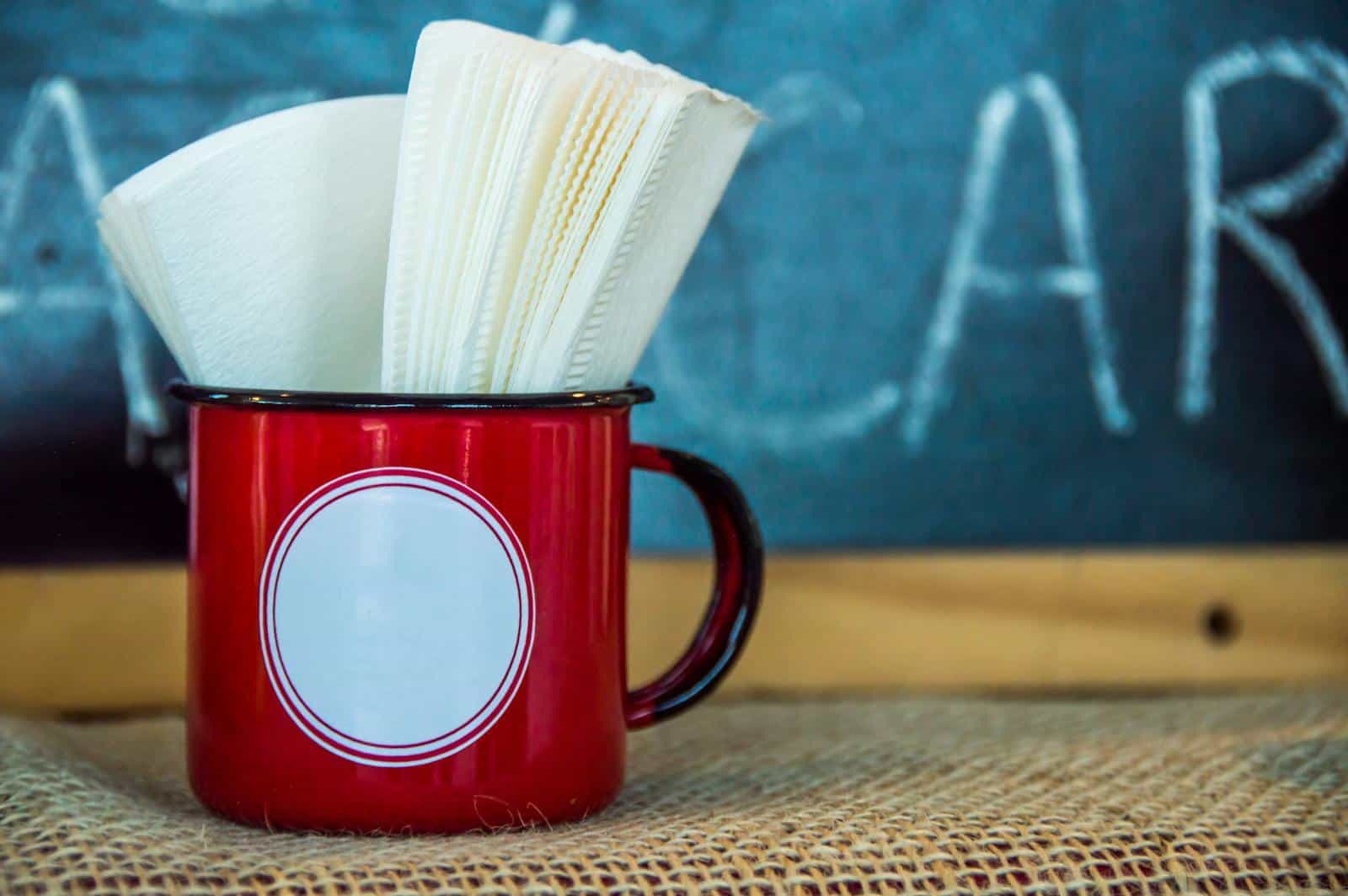 A vibrant red cup holding napkins set against a chalkboard background, perfect for cafe-themed imagery.