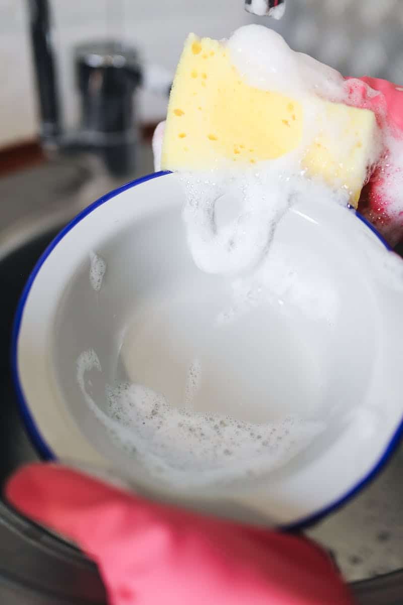 Vibrant photo of washing a bowl with a yellow sponge and soap bubbles.