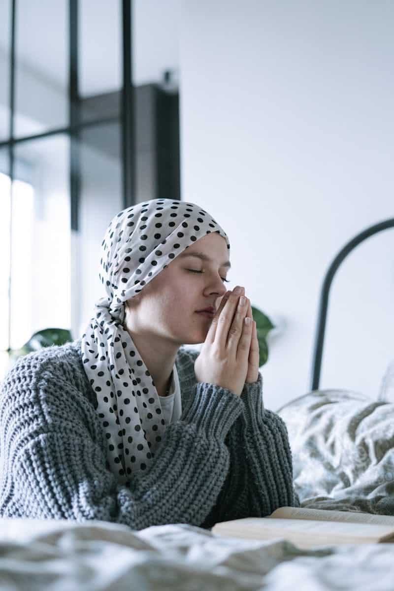 Woman wearing polka dot scarf, reflecting and praying, symbolizing hope and recovery.