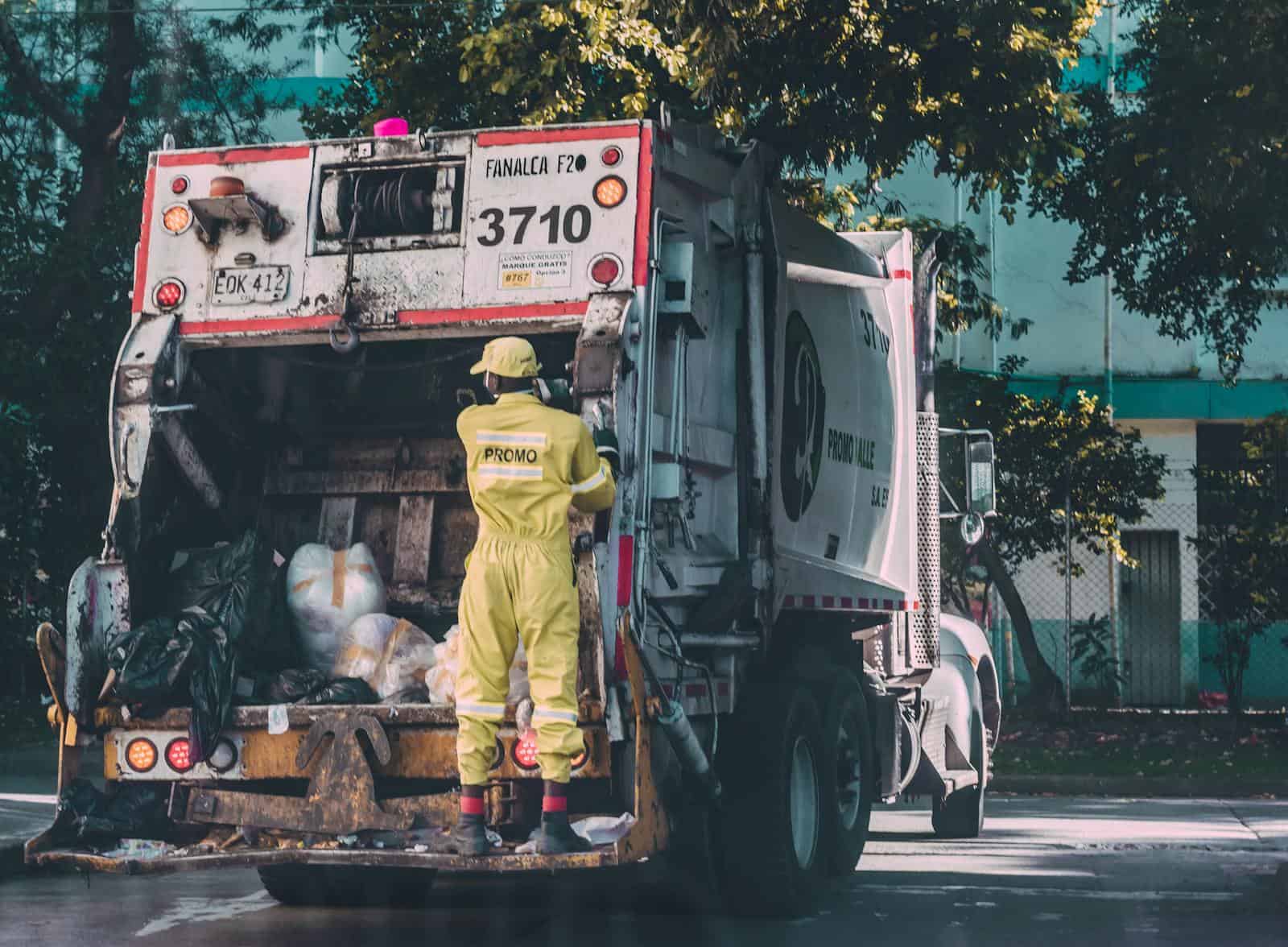 Sanitation worker collecting waste in Cali, Colombia. Urban scene with a garbage truck.