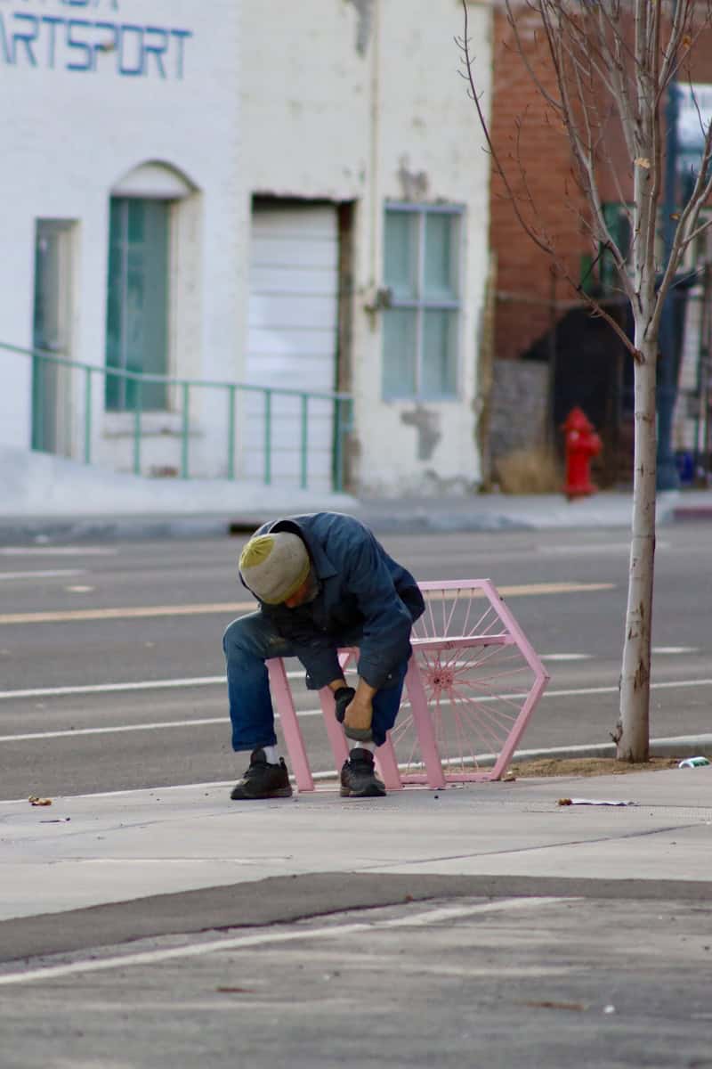 person in black jacket and yellow helmet riding pink kick scooter on sidewalk during daytime