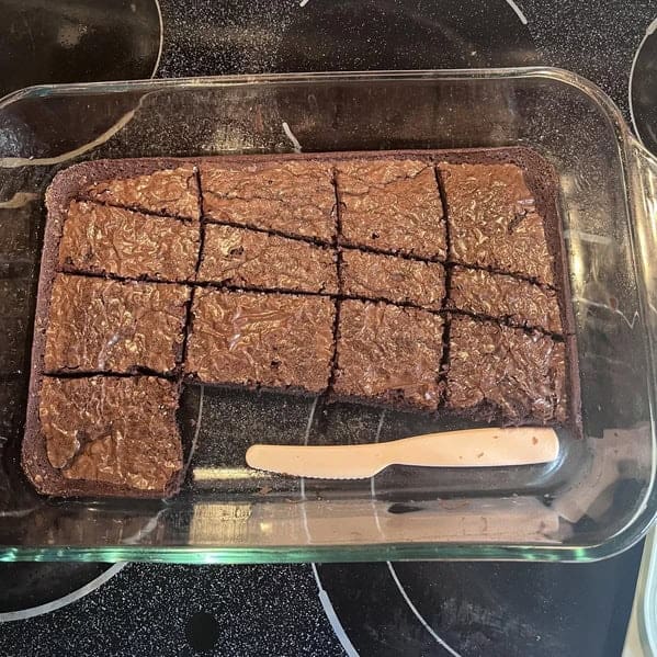 A square pan of brownies with a knife on top the brownies are poorly cut