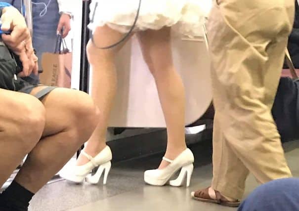Close-up of women's white high heels with pleated jeans at a fashion event.