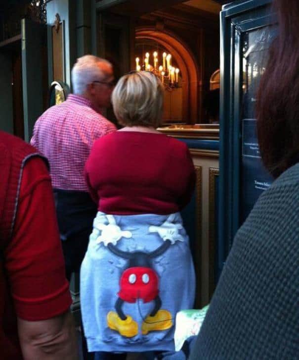 Woman wearing Pleated Jeans logo apron at a social event with others in a historic venue.