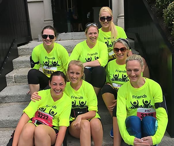 Group of women wearing neon green "Friends" shirts, sitting on steps after a race, smiling and celeb.