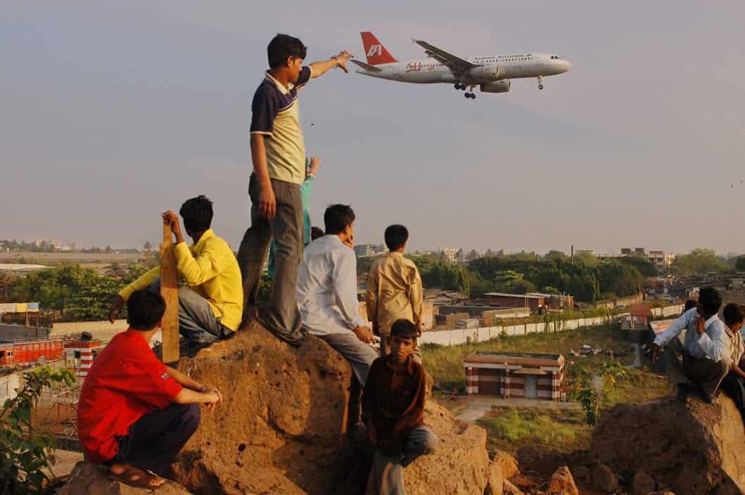 Children watching an airplane fly overhead from a hilltop in India.