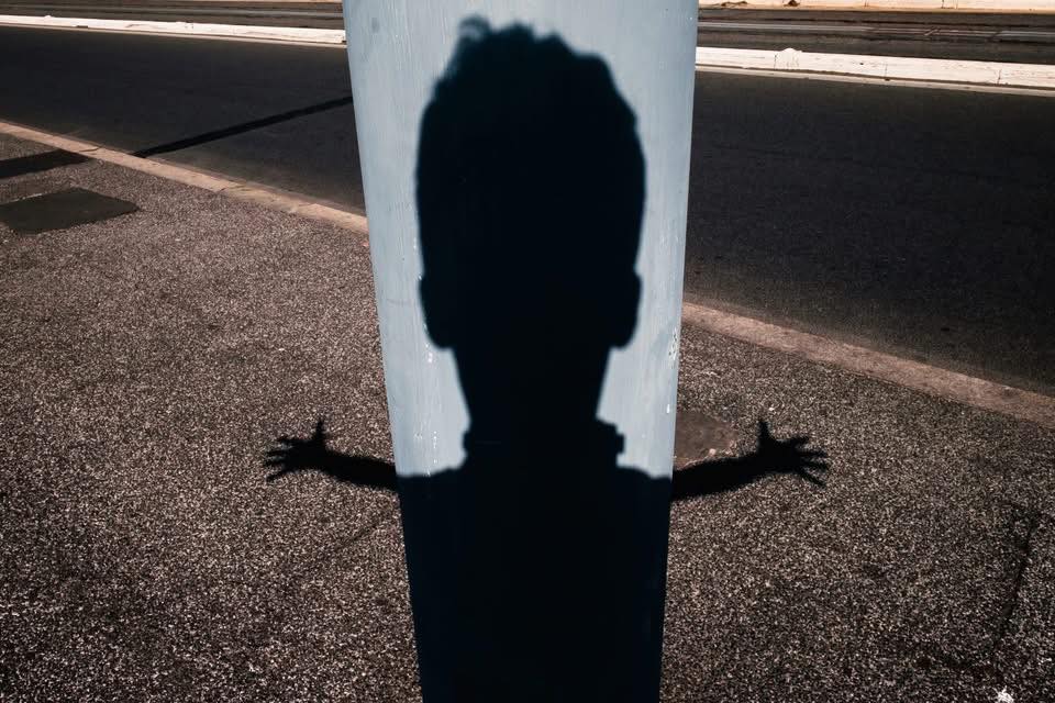 Shadow of a person with arms outstretched on a pole at night.