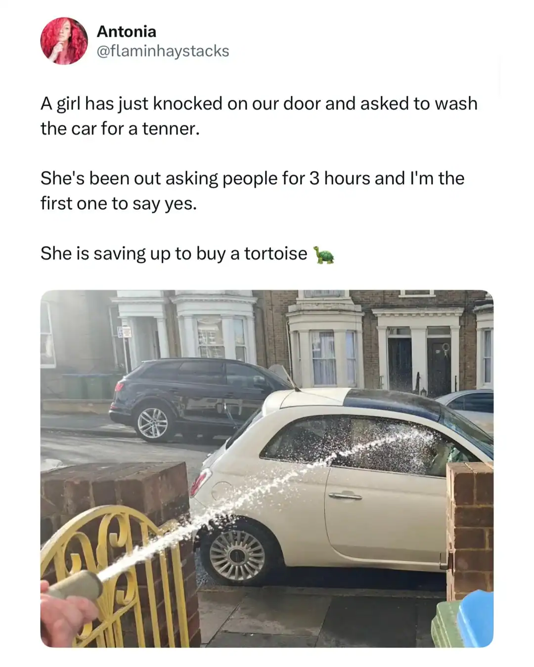 Girl spraying water on a parked white car with a garden hose on a city street.