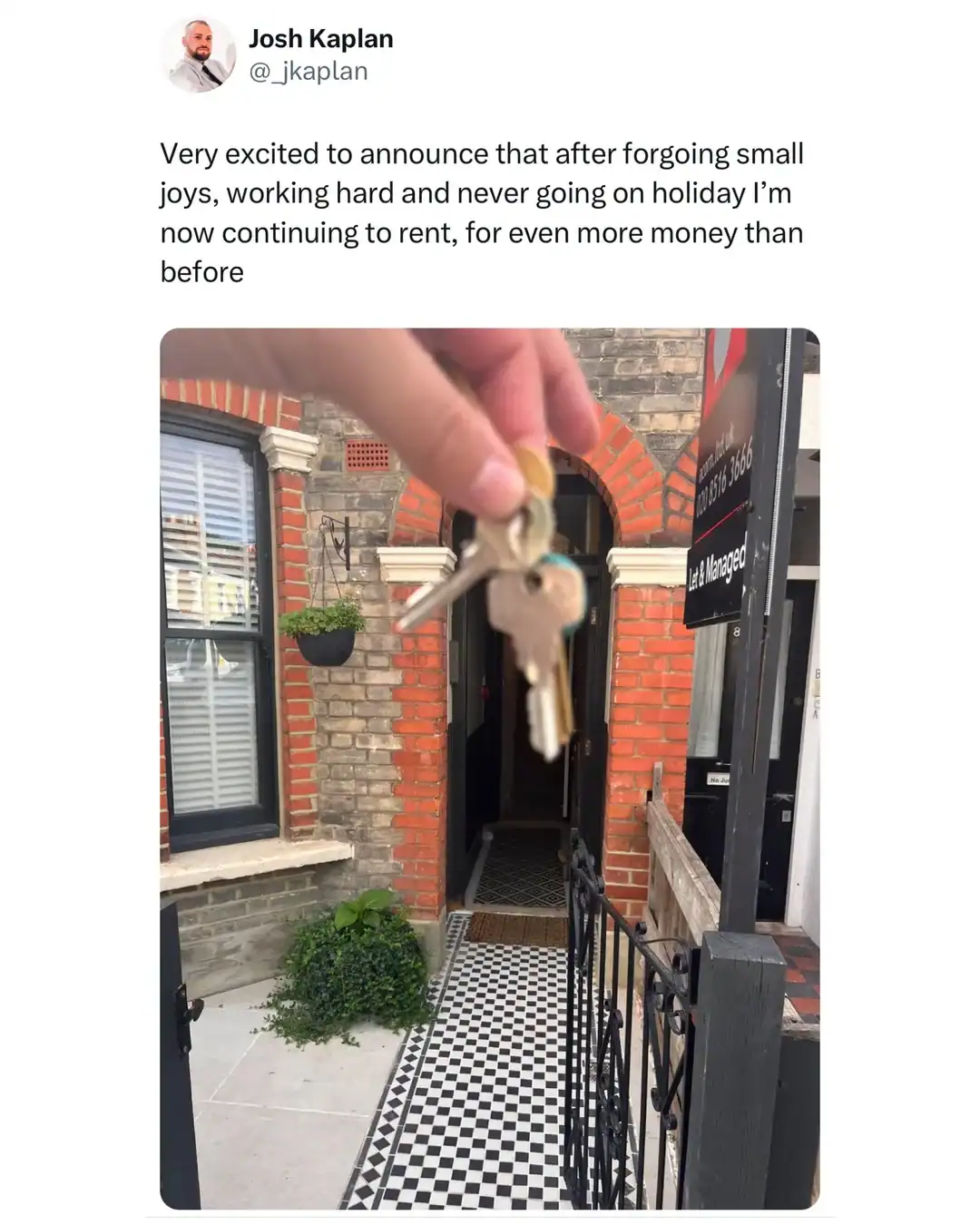 Hand holding keys outside a new apartment entrance with brick walls and checkered floor.