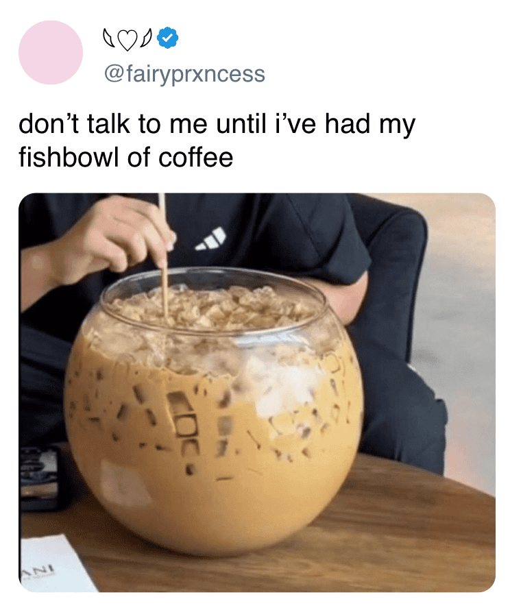 Person stirring a large fishbowl filled with iced coffee on a table.