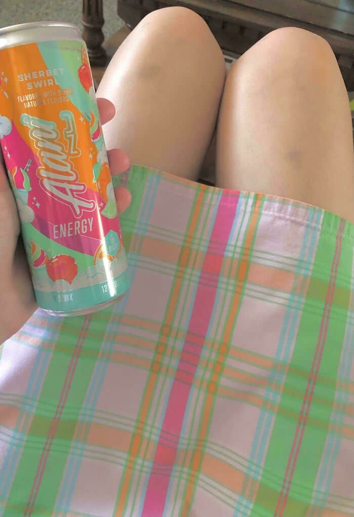 Person relaxing outdoors with a colorful drink and plaid skirt, summer leisure scene.