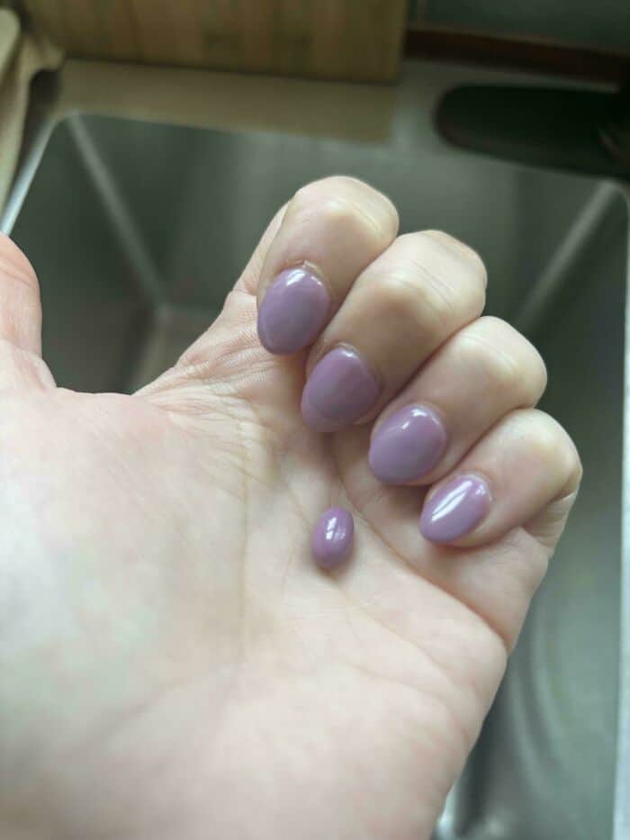 Close-up of a hand with lavender-colored, glossy, rounded nail polish on fingernails and a single sm.