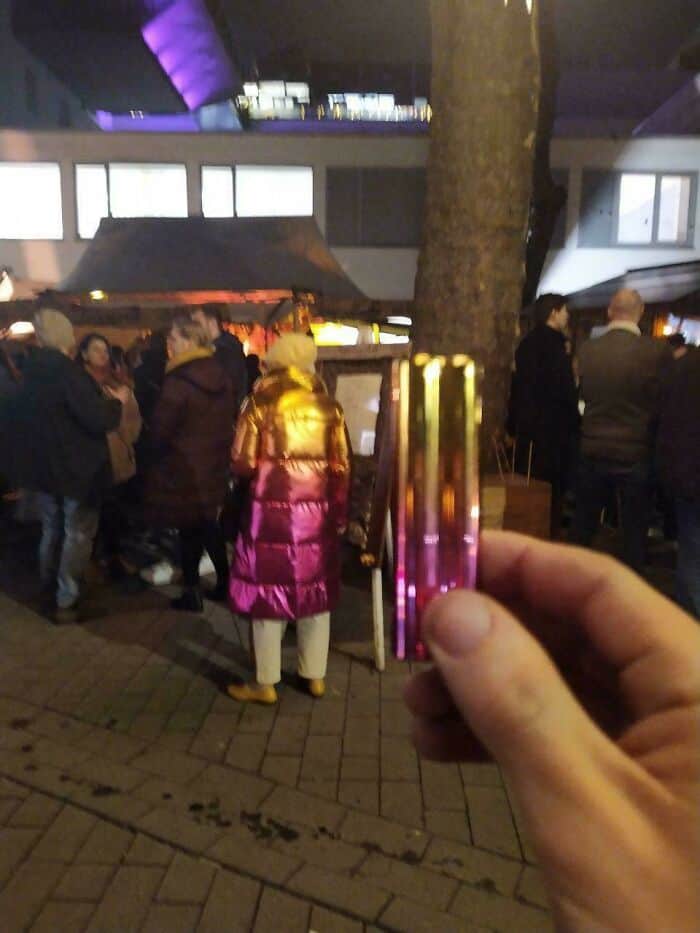 Hand holding a colorful pleated jeans card at night with a crowd in the background.