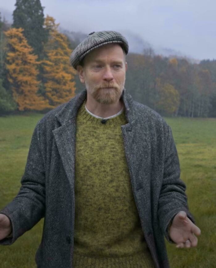 Man in a gray coat and flat cap standing outdoors in a foggy, autumn landscape.