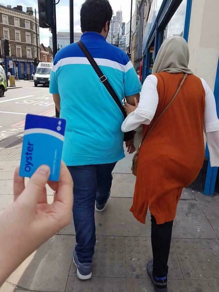 Two people walking on city sidewalk with a hand holding a blue Oyster card in the foreground.