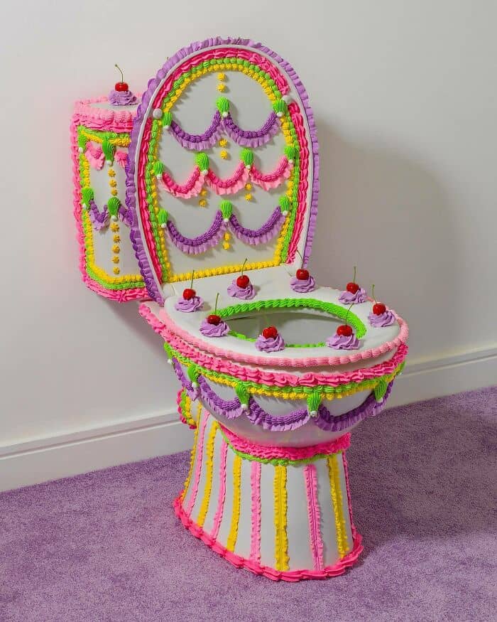 Toilet decorated with bright pink, purple, yellow, and green candies, resembling a whimsical cake.