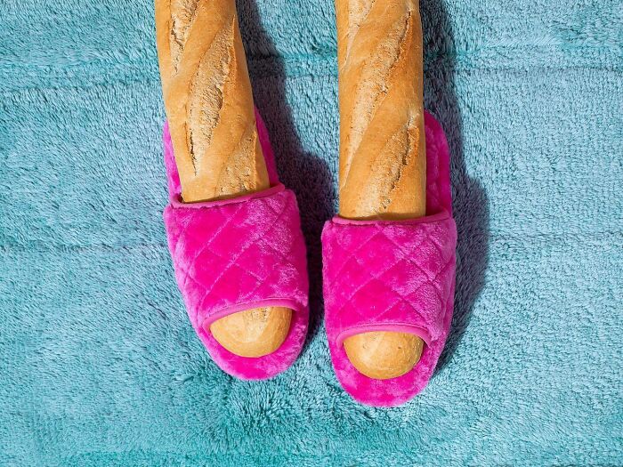 Surreal image of breadsticks wearing pink quilted slippers on a textured blue background.