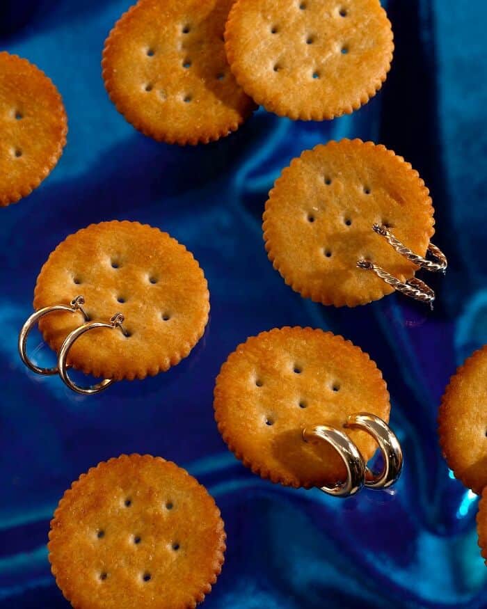 Cheese crackers with rings and earrings on a blue satin background.