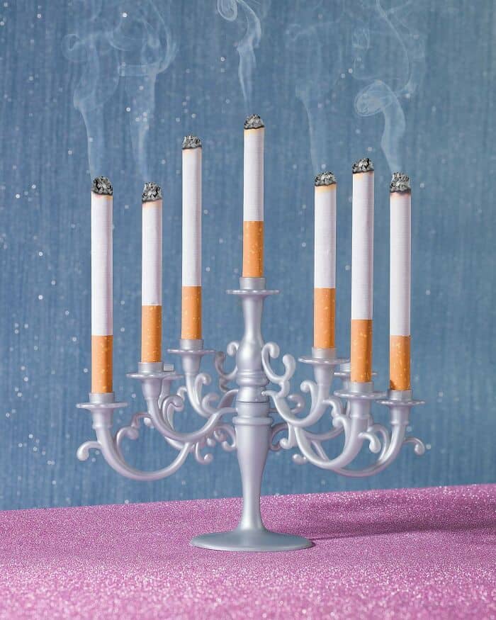Silver candelabra with burning cigarette candles on pink surface.