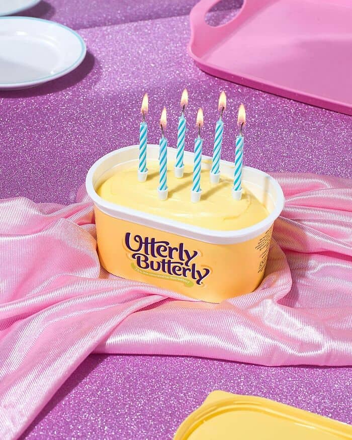 Surreal cake designed to look like a tub of Butterly Butterly ice cream with lit birthday candles, s.
