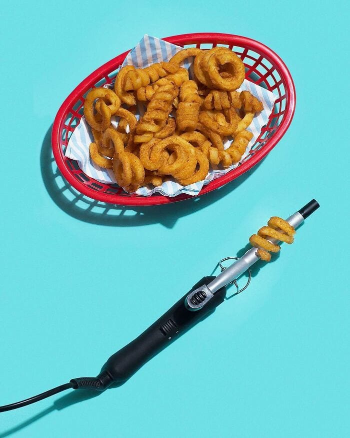 Basket of crispy onion rings on a blue background with a curling iron.
