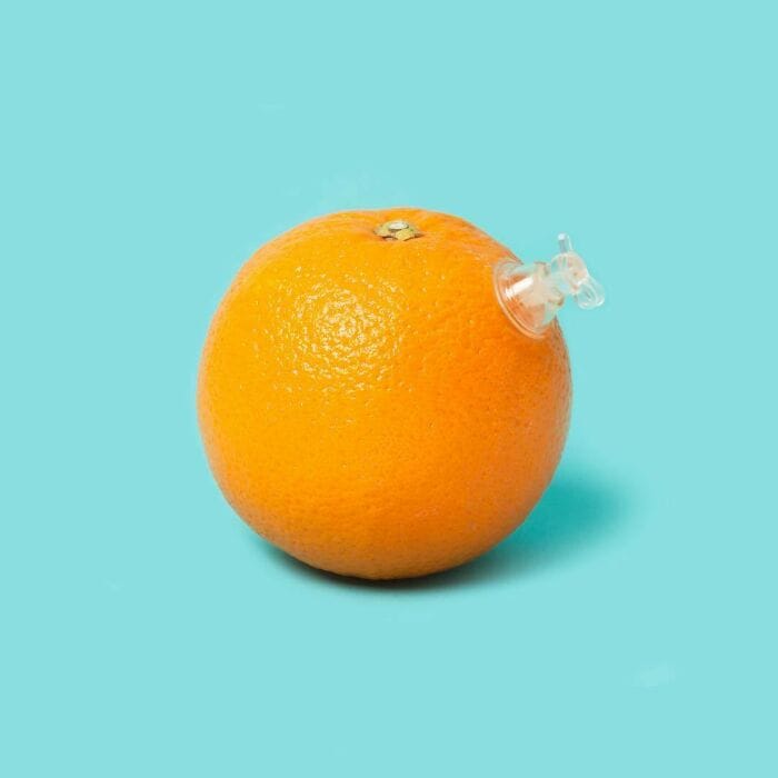 Orange with a syringe, surreal food art, humorous fruit display.