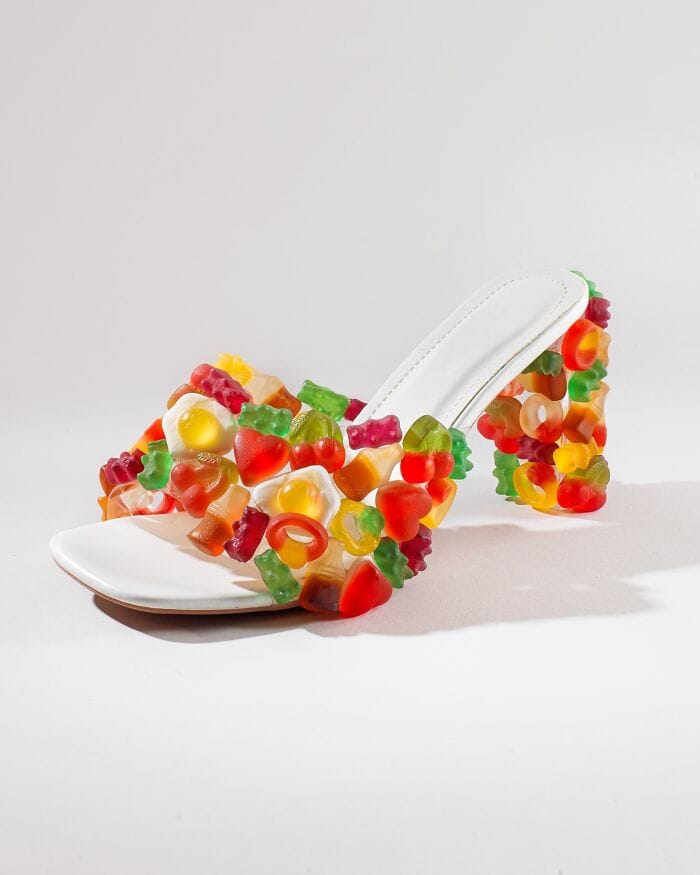 White high-heeled shoe covered in colorful gummy candies, playful and surreal.