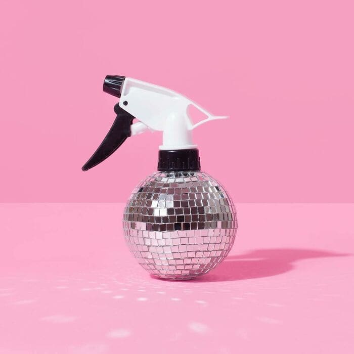Reflective disco ball spray bottle on pink background, surreal and humorous image.