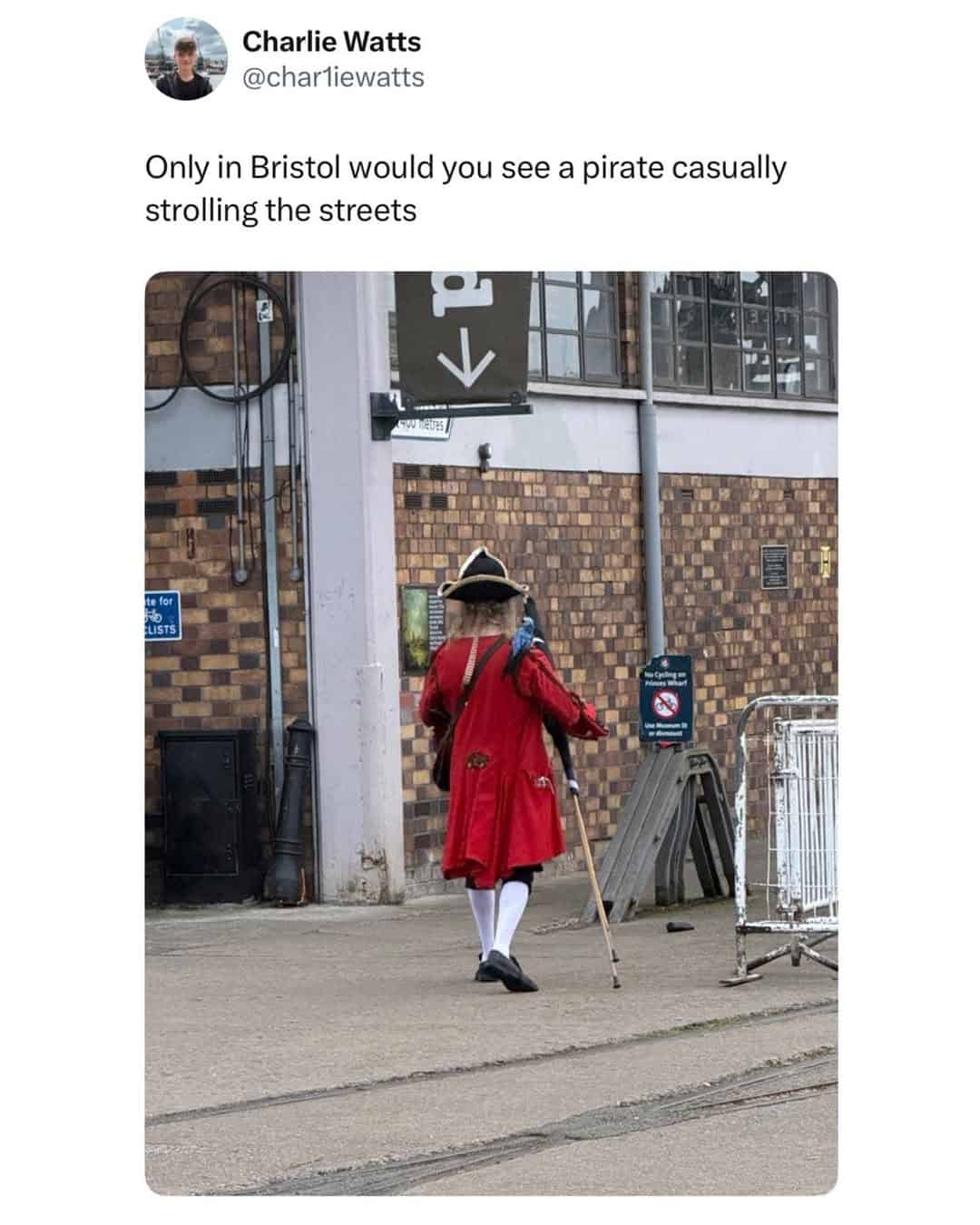 Pirate in a red coat, white stockings, and a tricorn hat, casually strolling with a cane in Bristol.