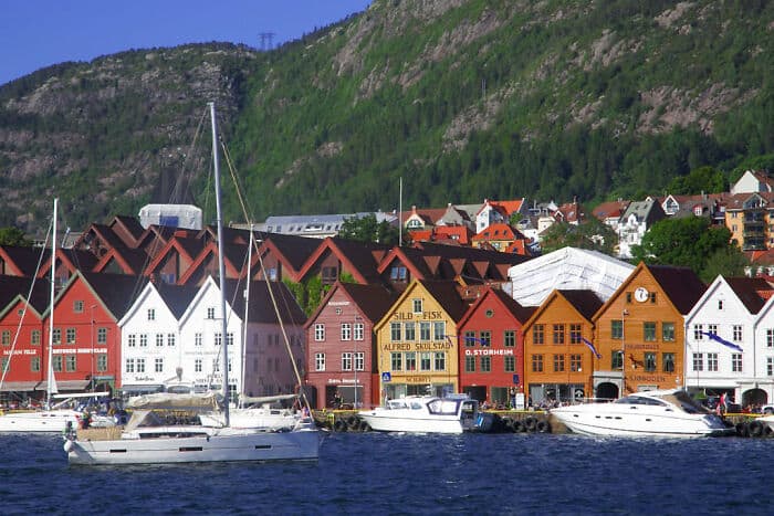 Colorful city harbor with boats, vibrant buildings, and scenic mountain backdrop.
