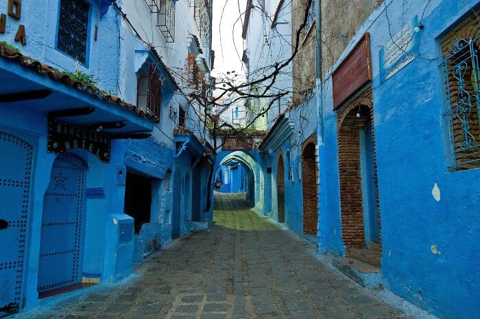Colorful blue alleyway with vibrant walls and arched doorways in a Moroccan city.