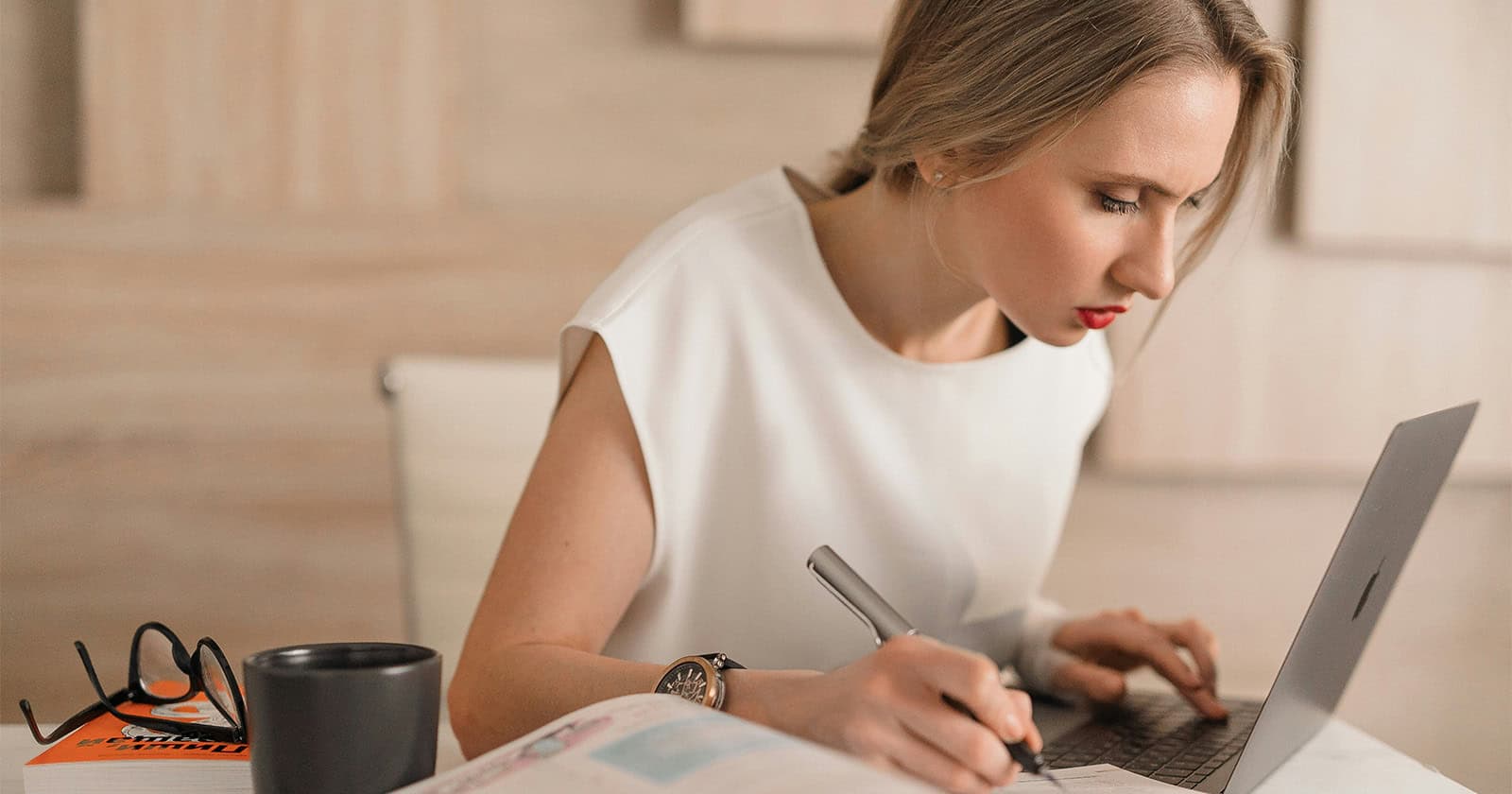 Woman working on a laptop with a technical manual and pen in an office setting.