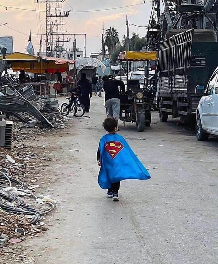 Young boy dressed as Superman walking through a busy market street.