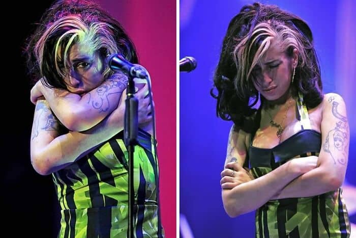 Female singer with colorful hair and tattoos singing passionately on stage with vibrant lighting.