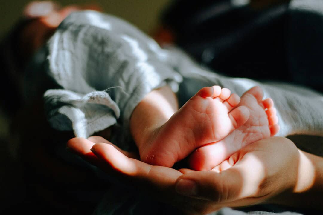Baby's tiny feet held gently in an adult's hand, symbolizing care and tenderness.