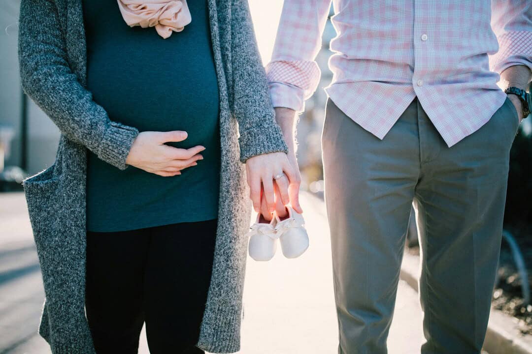 Pregnant woman and partner holding tiny baby shoes, symbolizing upcoming parenthood and family joy.