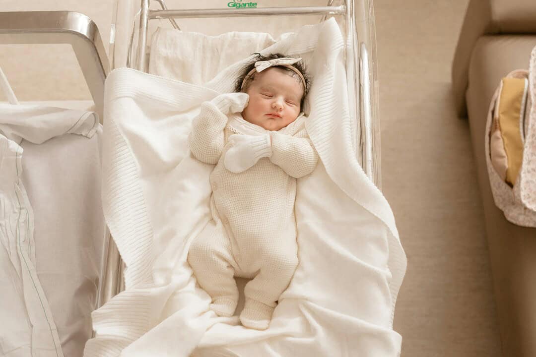 Baby sleeping peacefully in a hospital bassinet, wrapped in a cozy cream-colored outfit.