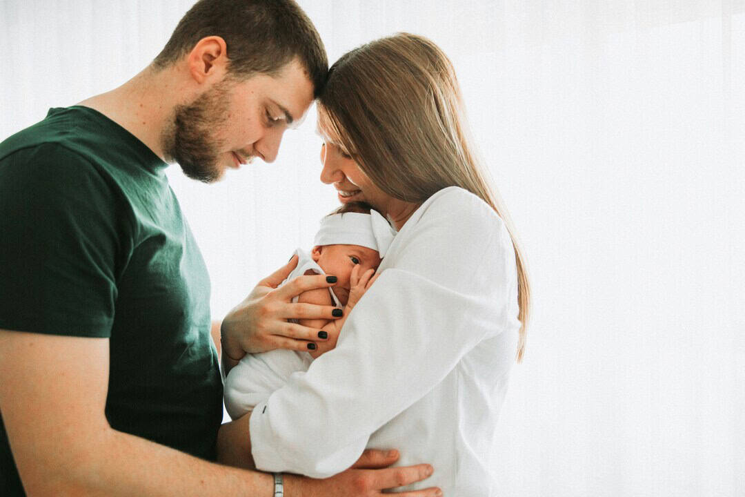 Young family holding newborn baby, smiling and loving in a bright, airy room.