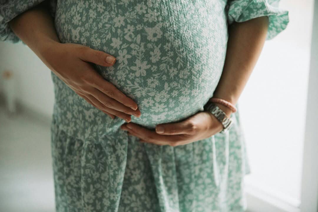 Pregnant woman in floral pajamas holding her belly, emphasizing maternity and prenatal care.