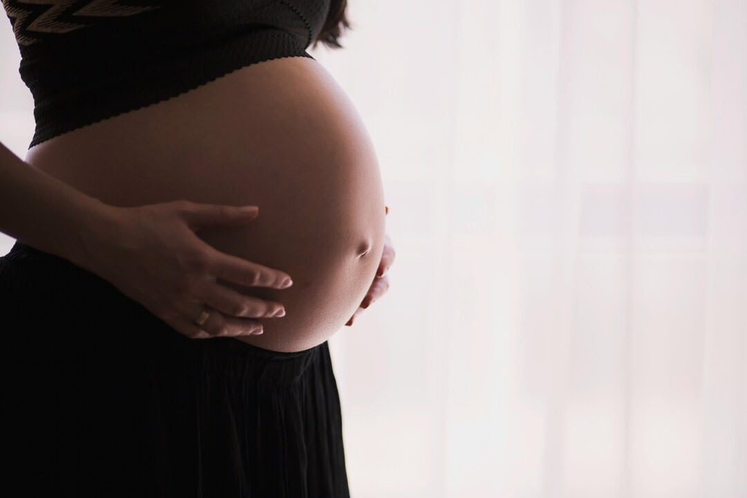 Pregnant woman gently holding her belly, showcasing pregnancy and maternal health.