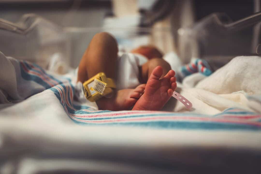 Close-up of a newborn baby's hand with hospital ID bracelet in incubator.