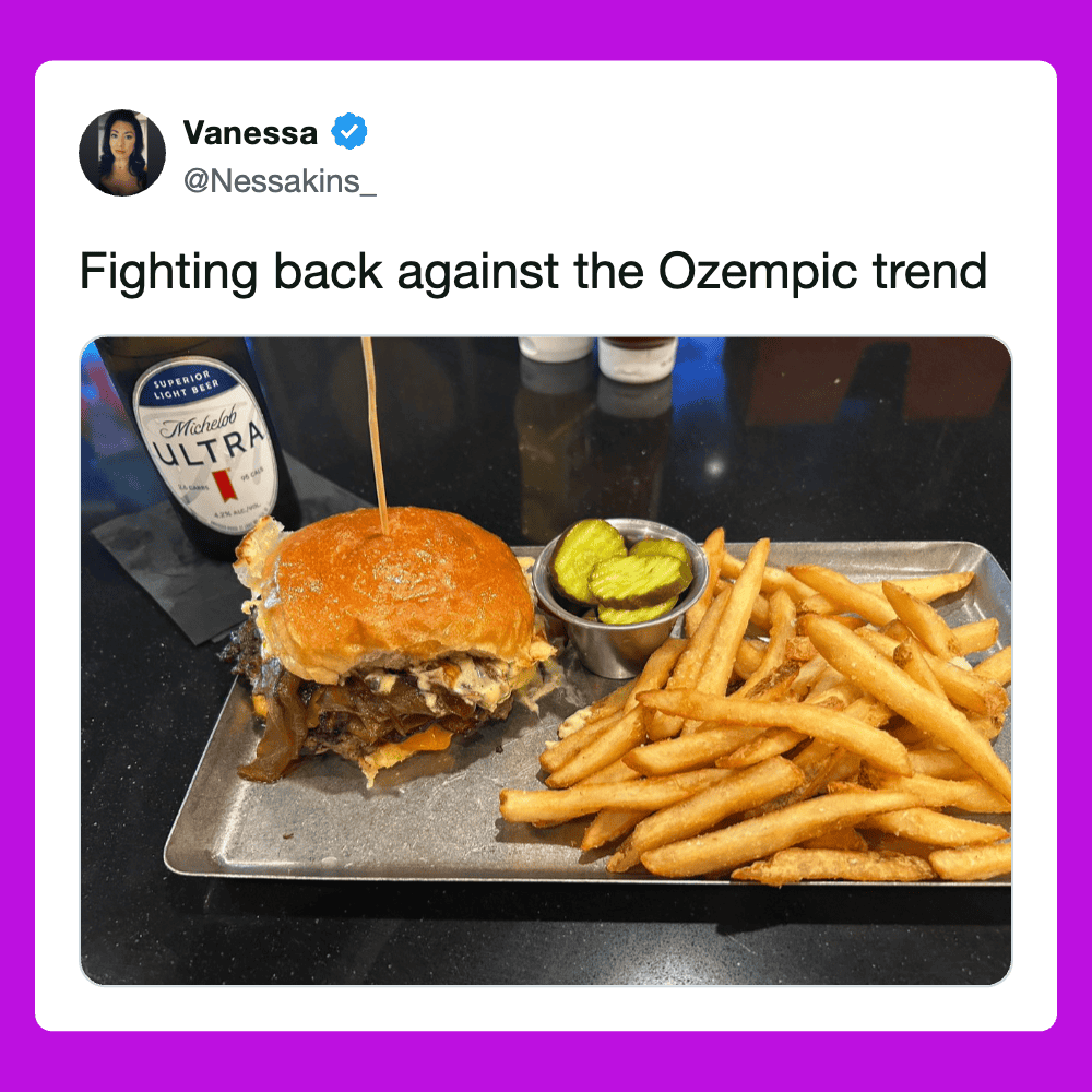 Cheeseburger with fries, pickles, and a beer on a metal tray, casual dining scene.
