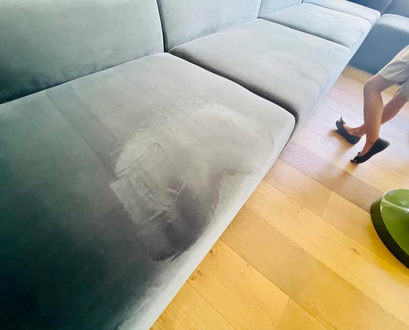 Soft gray sofa with visible stain on fabric, in a modern living room setting.