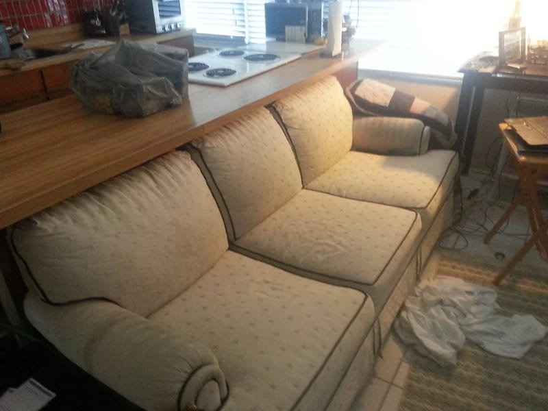 Comfortable beige sofa with plush cushions in a cozy living room, next to a kitchen counter and a wi.