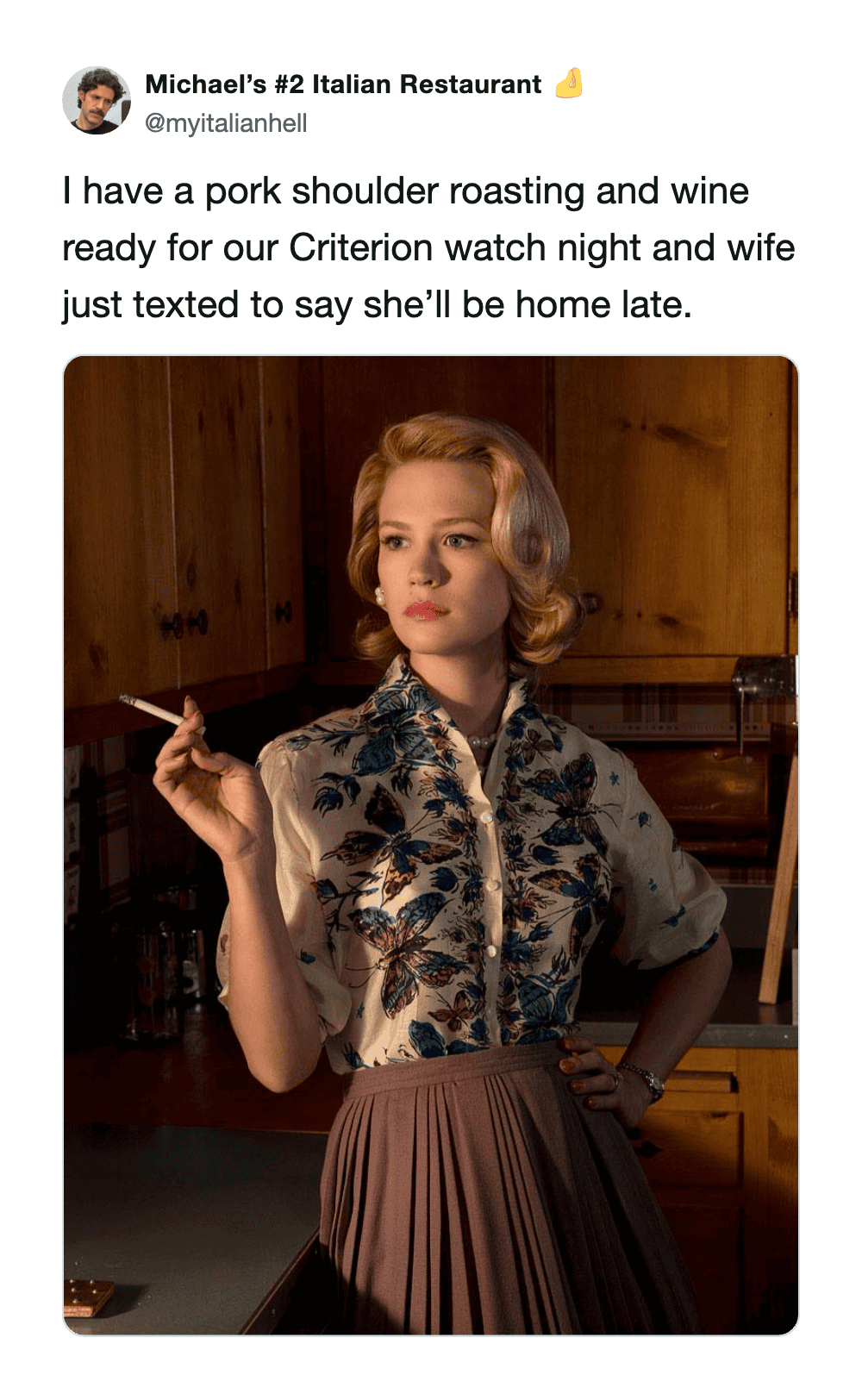 A woman with blonde hair in vintage attire holding a cigarette in a kitchen.